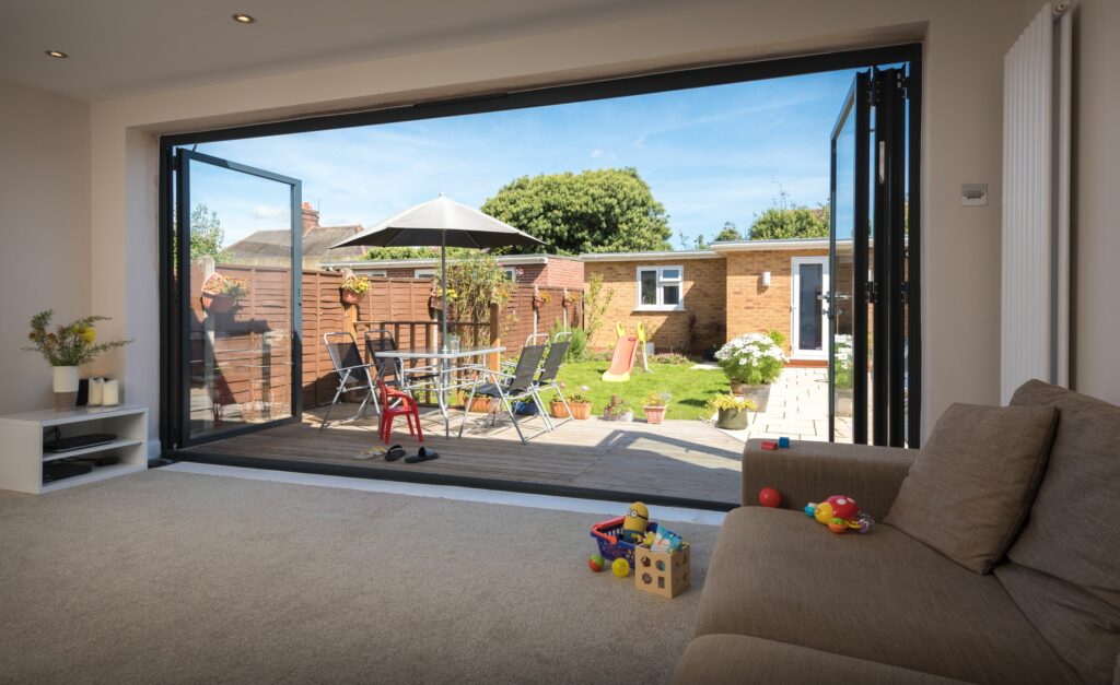 picture of trade supply bifold doors, opening out to a patio with a view of a garden room