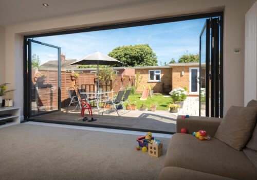 picture of trade supply bifold doors, opening out to a patio with a view of a garden room