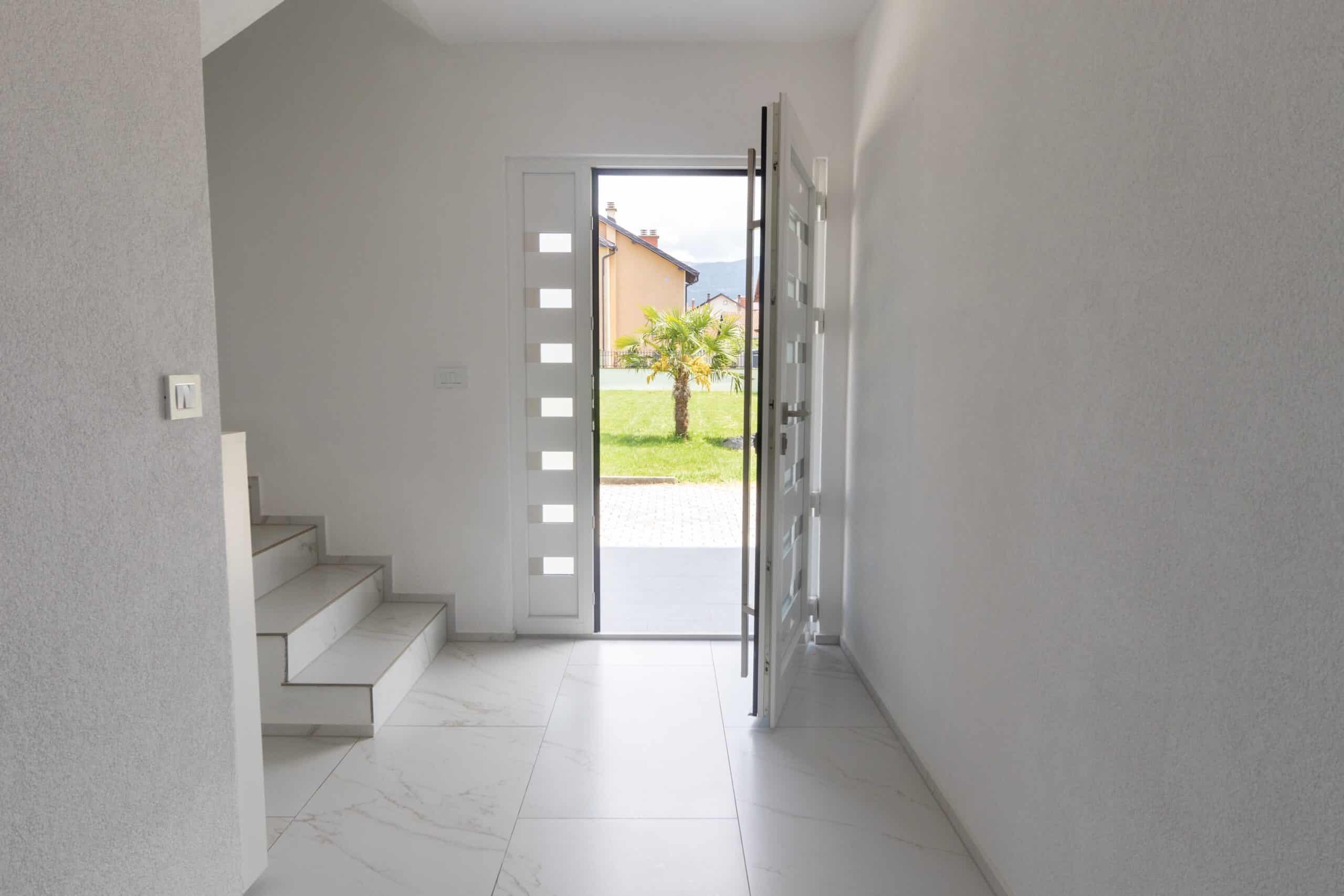 Reynaers CS77 front door White opened entrance door and marble tiled floor in front of green lawn with palm tree