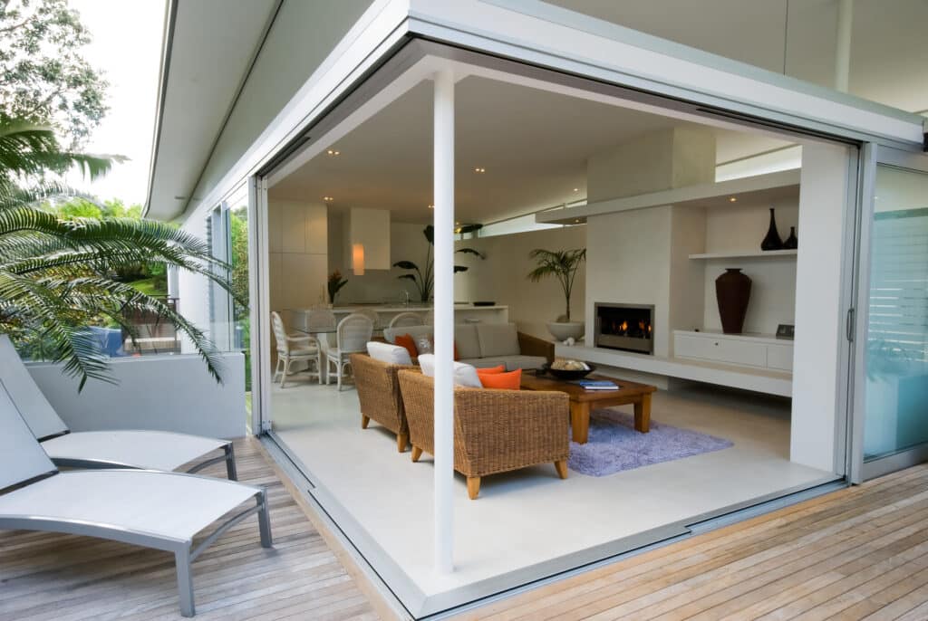 Reynaers sliding doors in an open corner design and white colour, open out to a patio. 